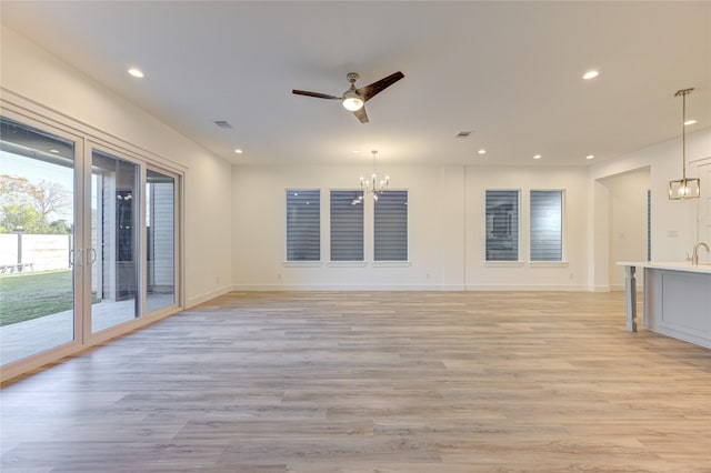 unfurnished living room featuring recessed lighting, visible vents, baseboards, light wood-style flooring, and ceiling fan with notable chandelier