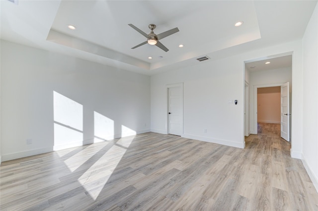 unfurnished room with a tray ceiling, baseboards, visible vents, and light wood finished floors