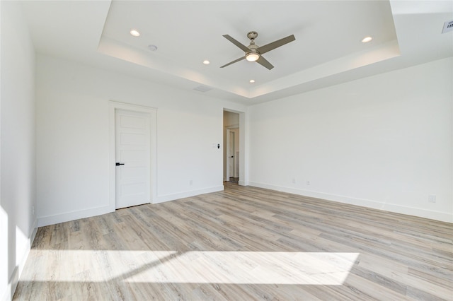 spare room with light wood-type flooring, a raised ceiling, and baseboards