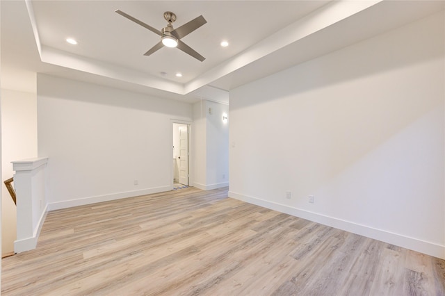 spare room with ceiling fan, recessed lighting, baseboards, light wood-style floors, and a tray ceiling