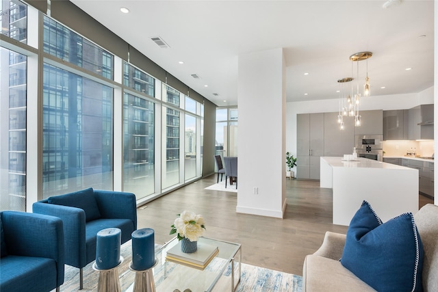 living room with visible vents, light wood-style flooring, an inviting chandelier, expansive windows, and recessed lighting