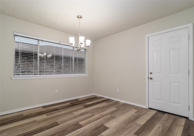 spare room with baseboards, a chandelier, and wood finished floors