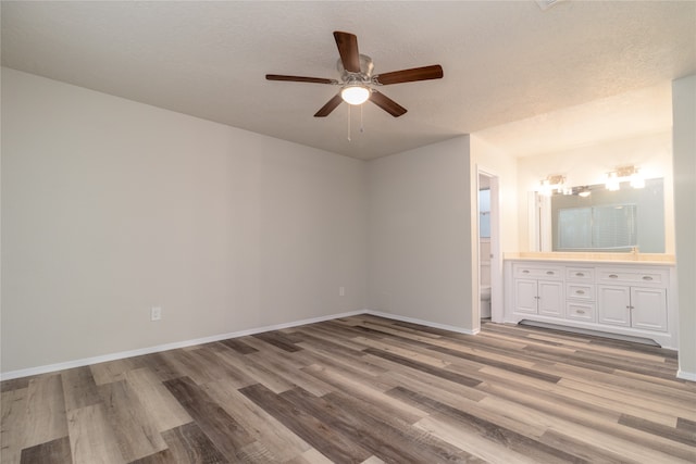 unfurnished bedroom featuring ensuite bath, a textured ceiling, baseboards, and wood finished floors