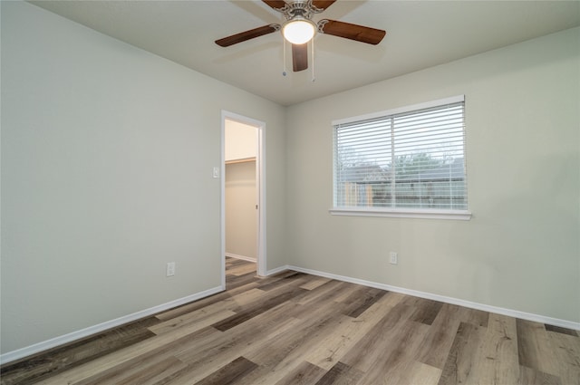 spare room featuring light wood finished floors, a ceiling fan, and baseboards