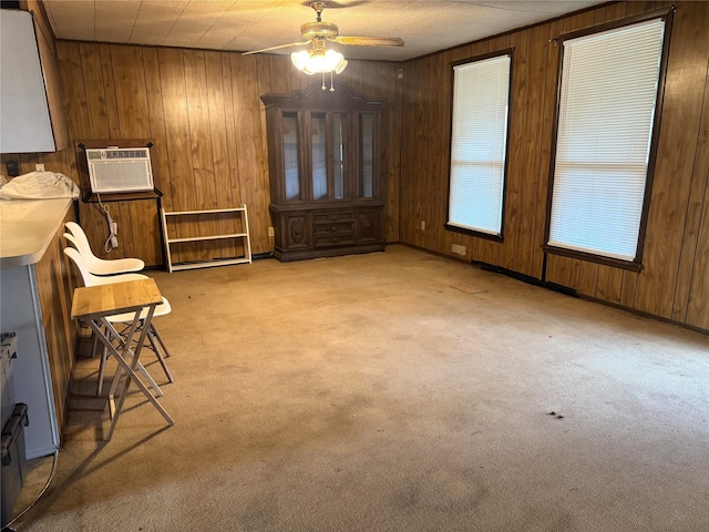 interior space with light carpet, wood walls, ceiling fan, and a wall mounted air conditioner