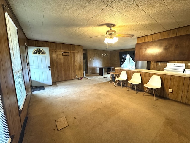 interior space with wood walls, ceiling fan, and light colored carpet