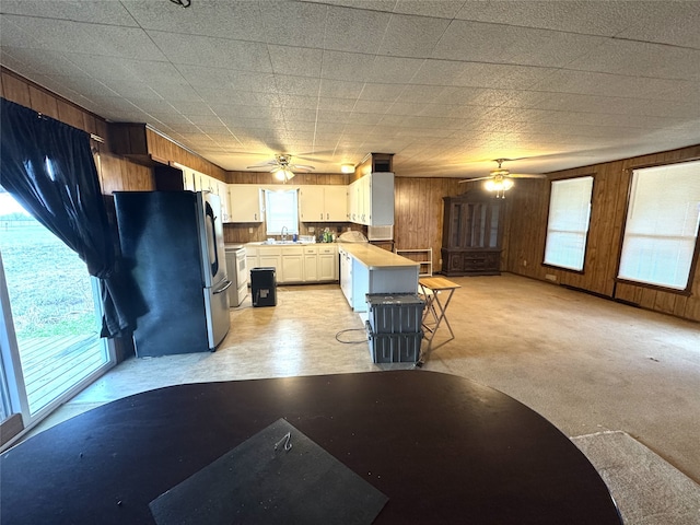 kitchen featuring freestanding refrigerator, open floor plan, white cabinets, wooden walls, and a kitchen breakfast bar