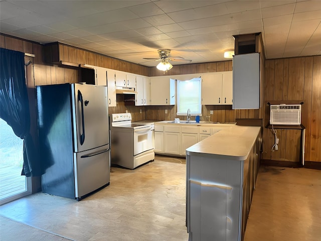 kitchen with electric range, freestanding refrigerator, light countertops, wood walls, and white cabinetry