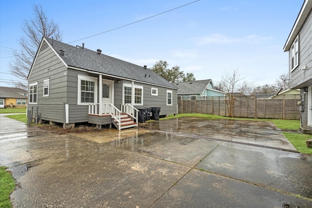 rear view of house featuring a shingled roof, fence, and a patio