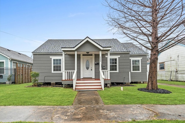 bungalow-style home with roof with shingles, fence, and a front lawn