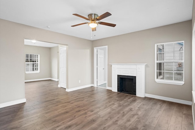 unfurnished living room with ceiling fan, a fireplace, dark wood finished floors, and baseboards