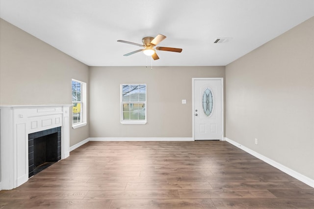 unfurnished living room with a fireplace, visible vents, dark wood-type flooring, a ceiling fan, and baseboards