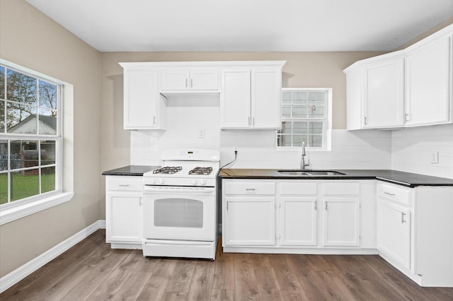 kitchen featuring dark countertops, a sink, white cabinets, and white range with gas cooktop