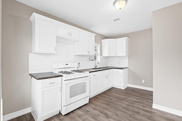 kitchen featuring white range with gas cooktop, baseboards, visible vents, white cabinetry, and a sink