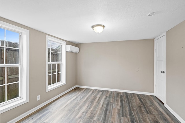 empty room with a textured ceiling, baseboards, dark wood-type flooring, and an AC wall unit