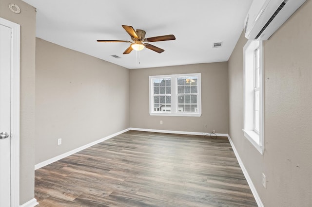 unfurnished room with a wealth of natural light, dark wood-style flooring, a wall mounted air conditioner, and visible vents