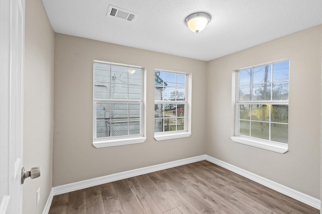 spare room with wood finished floors, visible vents, and baseboards