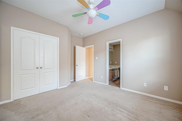 unfurnished bedroom with a closet, ensuite bathroom, light carpet, ceiling fan, and baseboards