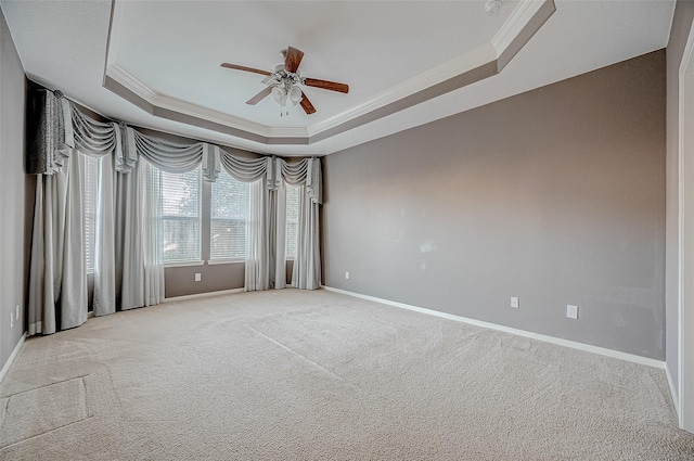 spare room featuring light colored carpet, a ceiling fan, baseboards, ornamental molding, and a raised ceiling