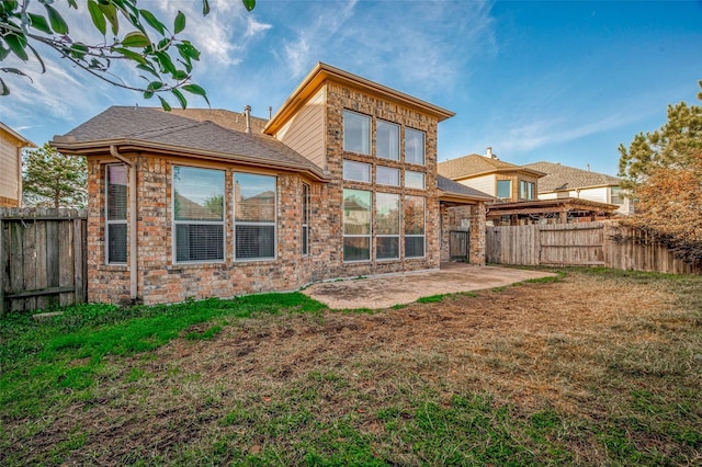 back of house featuring a fenced backyard, brick siding, a yard, roof with shingles, and a patio area