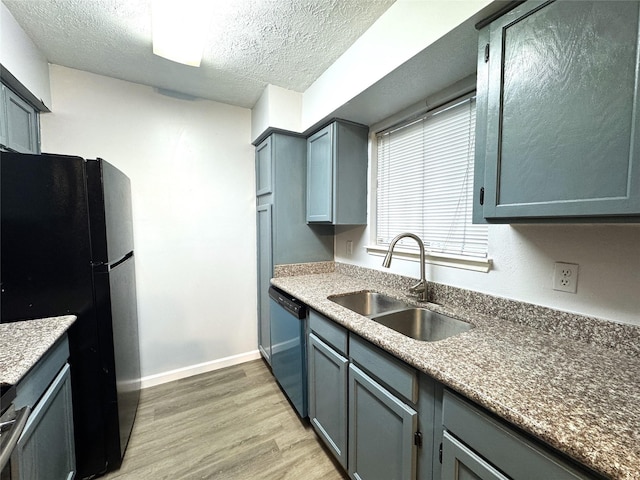 kitchen featuring light wood finished floors, dishwasher, freestanding refrigerator, a textured ceiling, and a sink