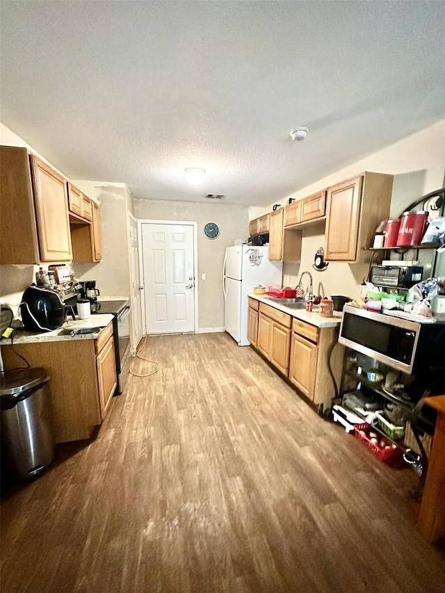 kitchen with light countertops, stainless steel microwave, freestanding refrigerator, a sink, and light wood-type flooring