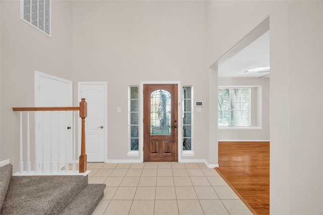 entryway featuring light tile patterned floors, baseboards, visible vents, a towering ceiling, and stairway