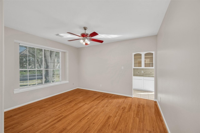 spare room with ceiling fan, light wood-type flooring, visible vents, and baseboards