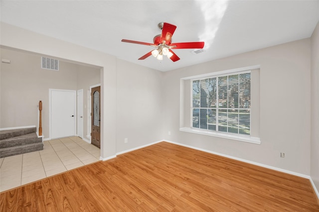 empty room with ceiling fan, stairway, light wood-type flooring, and visible vents