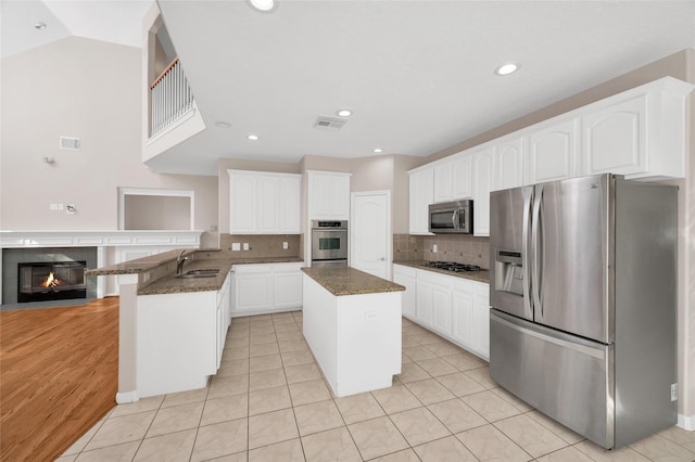 kitchen featuring stainless steel appliances, dark stone counters, a center island, and a sink