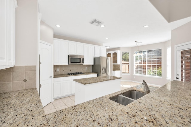 kitchen featuring appliances with stainless steel finishes, a center island, light stone countertops, pendant lighting, and a sink