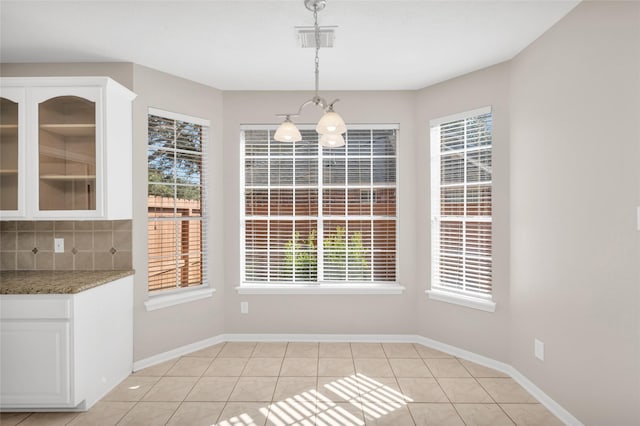 unfurnished dining area featuring light tile patterned floors, baseboards, visible vents, and a chandelier