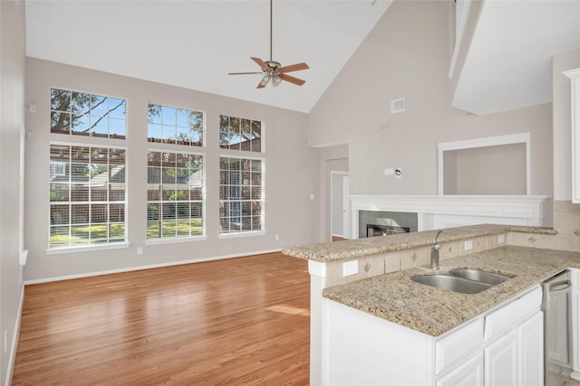 kitchen featuring light wood finished floors, white cabinets, open floor plan, a fireplace, and a sink