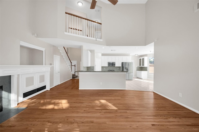 unfurnished living room featuring a tile fireplace, light wood-style flooring, a ceiling fan, baseboards, and stairway