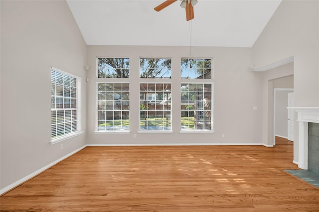 interior space featuring a healthy amount of sunlight, light wood-style flooring, high vaulted ceiling, and a tiled fireplace