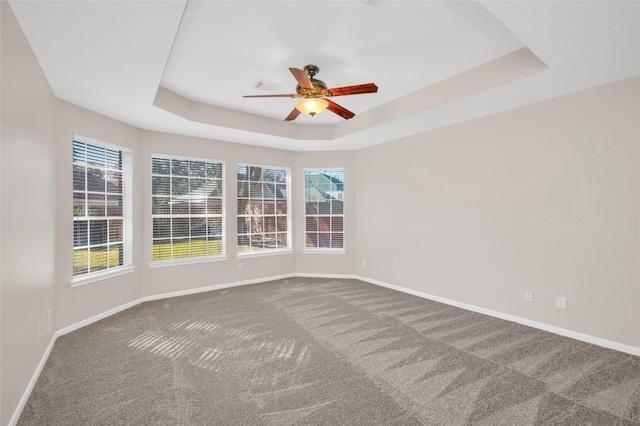 carpeted empty room featuring baseboards, a raised ceiling, and a ceiling fan