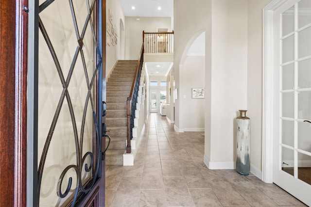 entrance foyer featuring arched walkways, light tile patterned flooring, recessed lighting, a towering ceiling, and baseboards