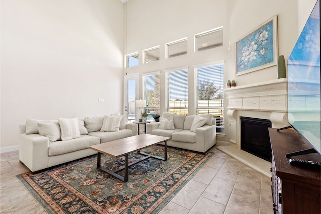 living room featuring a high ceiling, light tile patterned flooring, a glass covered fireplace, and baseboards