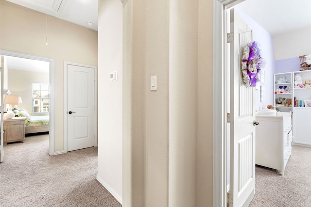 corridor featuring light carpet, attic access, and baseboards