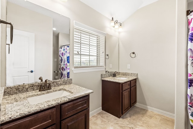 full bath with two vanities, a sink, and baseboards