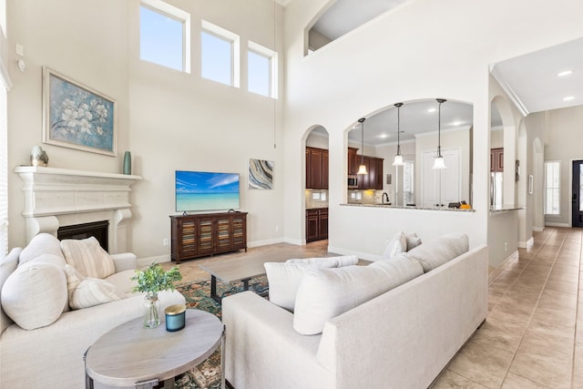 living area with arched walkways, a fireplace, a towering ceiling, baseboards, and ornamental molding