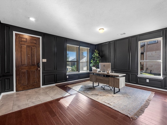 home office featuring light wood-style floors, visible vents, a decorative wall, and a textured ceiling