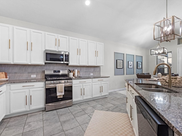 kitchen featuring white cabinets, dark stone countertops, hanging light fixtures, stainless steel appliances, and a sink