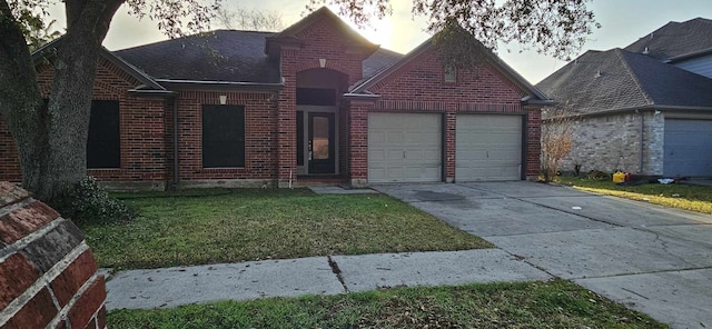 view of front of property with a garage, brick siding, a lawn, and driveway