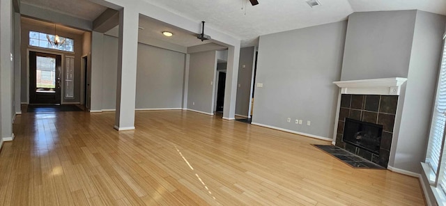 unfurnished living room featuring ceiling fan, wood finished floors, baseboards, vaulted ceiling, and a tiled fireplace