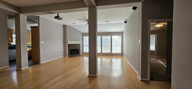 unfurnished living room with a ceiling fan, baseboards, a fireplace, and light wood finished floors