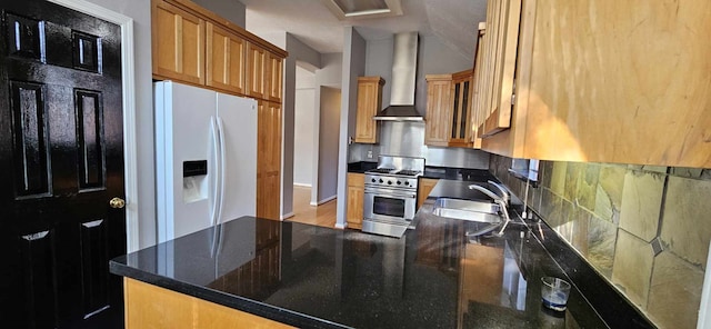 kitchen featuring white refrigerator with ice dispenser, a sink, wall chimney range hood, brown cabinets, and stainless steel range