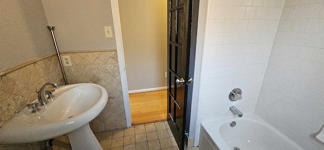 bathroom featuring a sink, washtub / shower combination, tile walls, and wainscoting