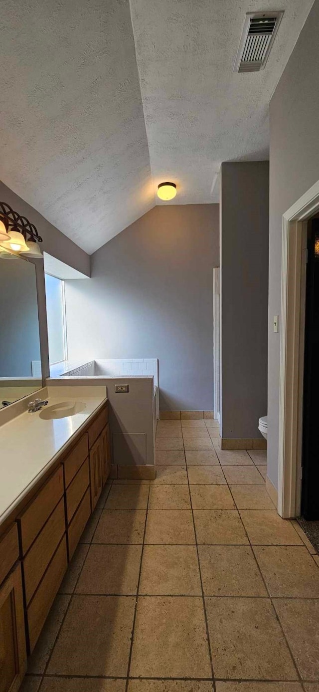 bathroom featuring visible vents, toilet, vaulted ceiling, a textured ceiling, and a sink