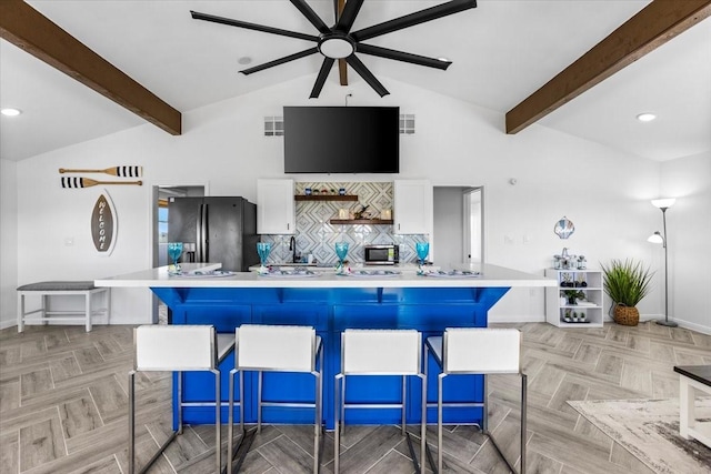 kitchen with tasteful backsplash, freestanding refrigerator, white cabinets, light countertops, and vaulted ceiling with beams